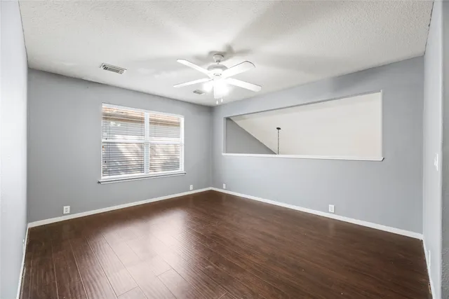 an empty room with wooden floor chandelier fan and windows