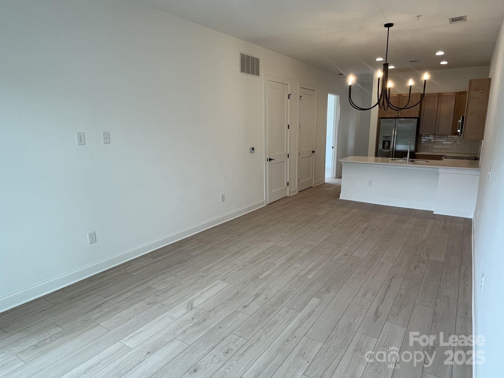 19546 Greentree Way, Unit 201 Cornelius, NC 28031 - Photo 14 of 31 an empty room with wooden floor a kitchen view and a chandelier