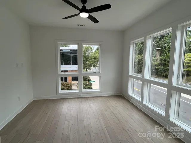 an empty room with wooden floor fan and windows