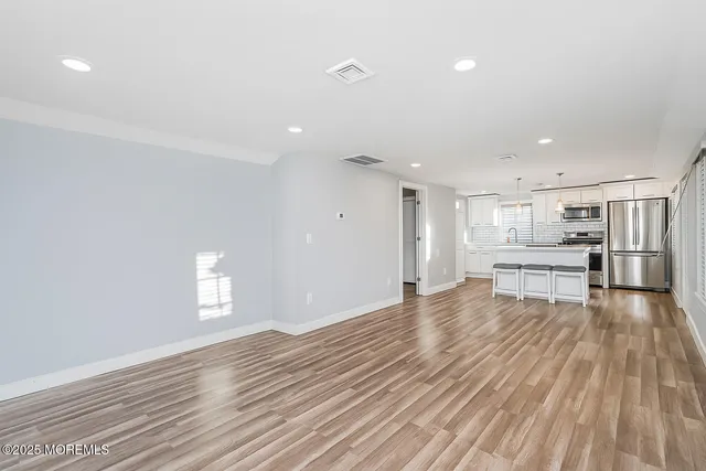 a view of kitchen and empty room with wooden floor