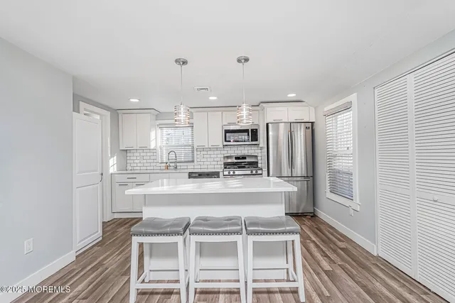 a view of a kitchen with kitchen island a sink wooden floor and stainless steel appliances