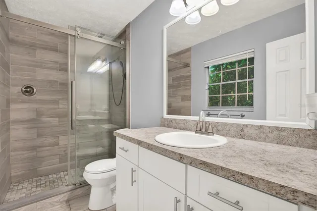 a bathroom with a granite countertop sink a toilet a mirror and shower
