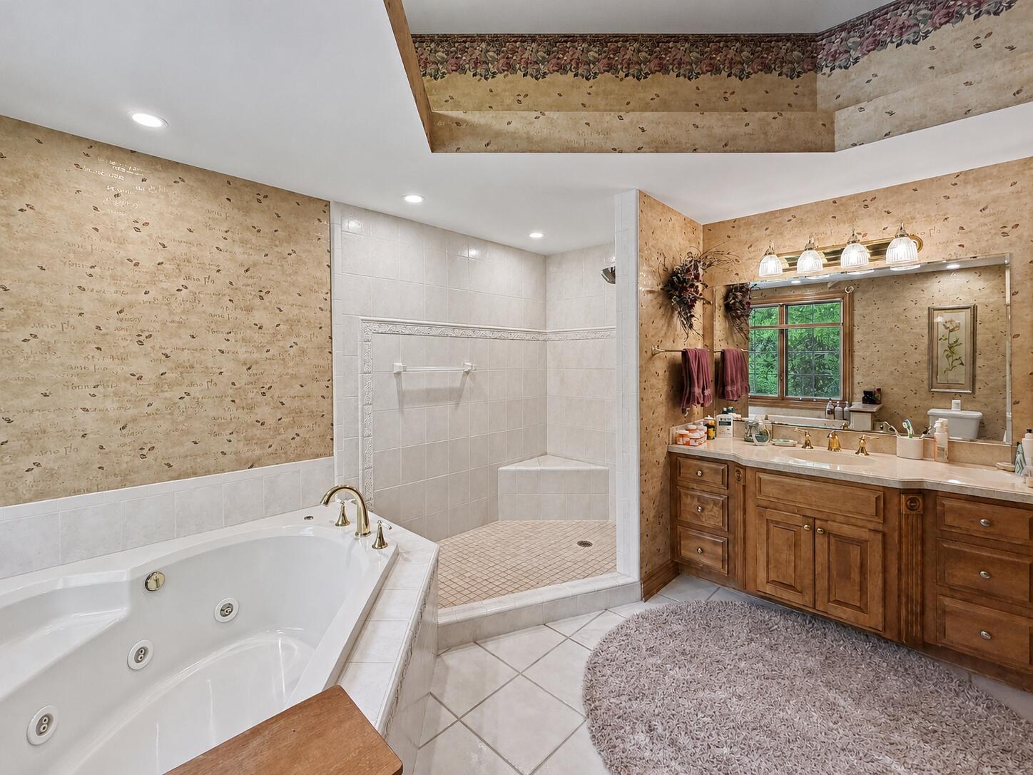 W291-s5245 Ridgefield Road Waukesha, WI 53189 - Photo 21 of 44 The expansive primary suite offers a stunning tray ceiling, serene wooded views, and generous space for furnishings and relaxation. The luxurious ensuite bath features a whirlpool soaking tub, oversized walk-in shower, dual-sink vanity, and spacious walk-in closet, creating a true private retreat.