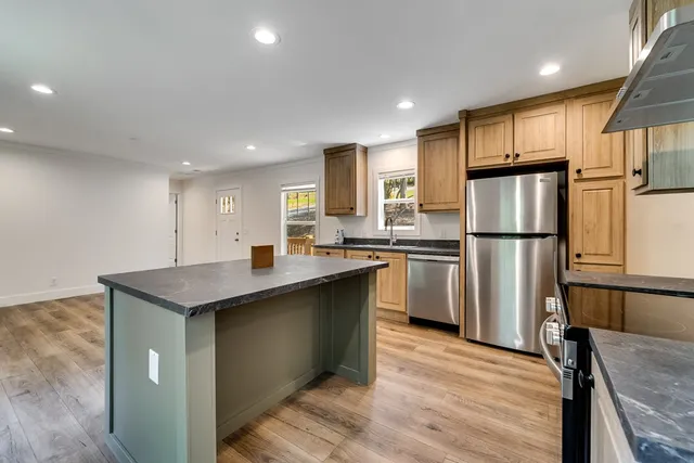 a kitchen with stainless steel appliances granite countertop a refrigerator a sink dishwasher a s stove top oven a large island with wooden cabinets and wooden floor