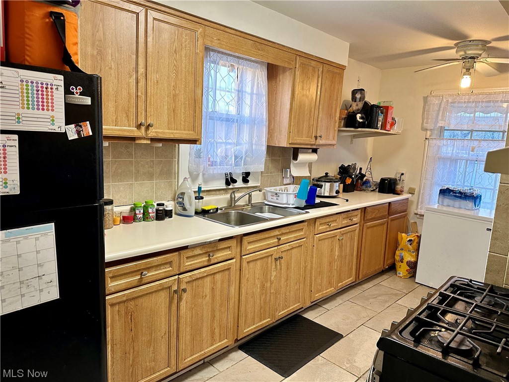 4197 Lambert Road Cleveland, OH 44121 - Photo 3 of 13 Kitchen featuring tasteful backsplash, sink, light tile floors, black fridge, and ceiling fan