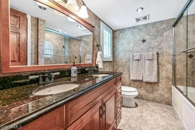a bathroom with a granite countertop sink a toilet a mirror and shower