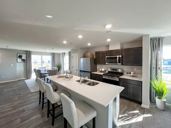 a kitchen with stainless steel appliances kitchen island granite countertop a dining table chairs and a refrigerator