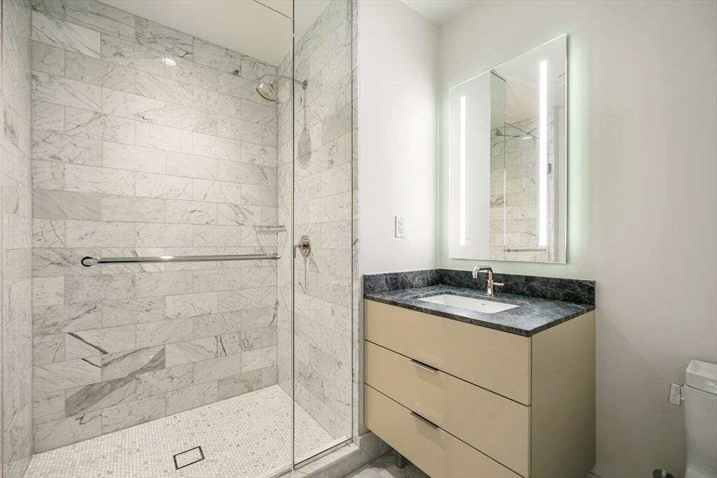240 Devonshire Street, Unit 4706 Boston, MA 02110 - Photo 12 of 40 a bathroom with a granite countertop sink a mirror and shower