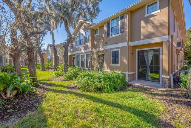 a view of a house with brick walls plants and large tree