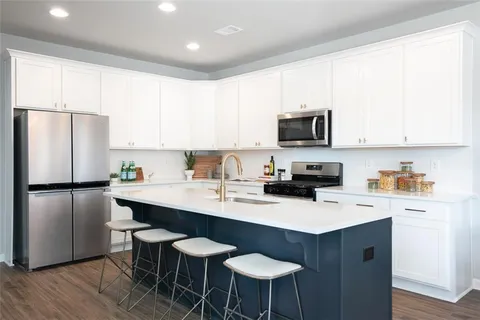 a kitchen with a refrigerator a stove a sink and white cabinets with wooden floor