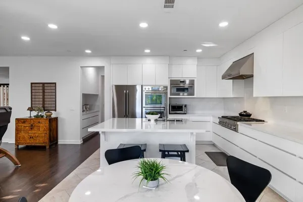 a large white kitchen with stainless steel appliances granite countertop a stove a sink a dining table and chairs