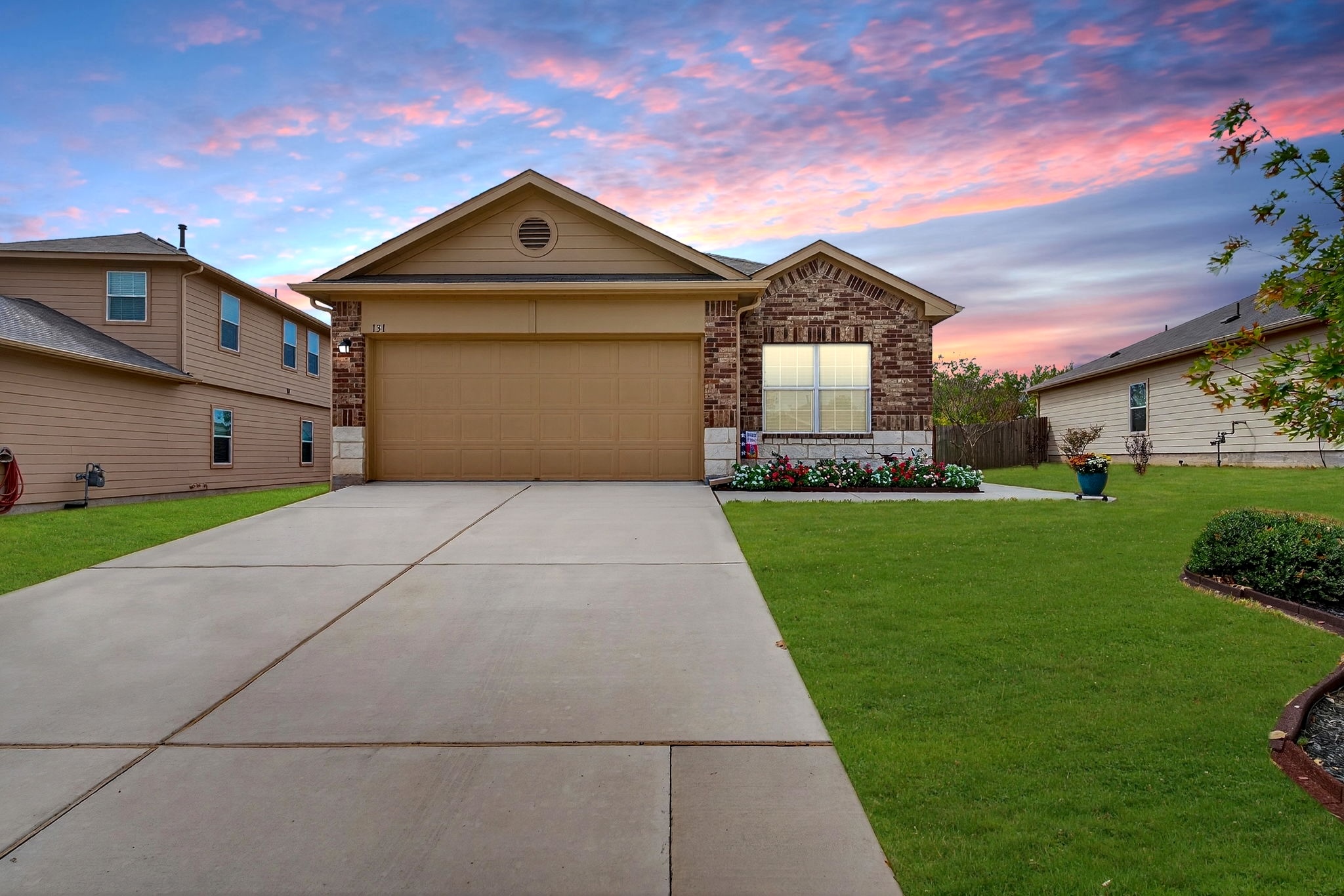 131 Coleto Creek Loop Kyle, TX 78640 - Photo 2 of 30 View of front of house featuring brick siding, driveway, and an attached garage. Virtually Staged twilight and green grass enhancement.