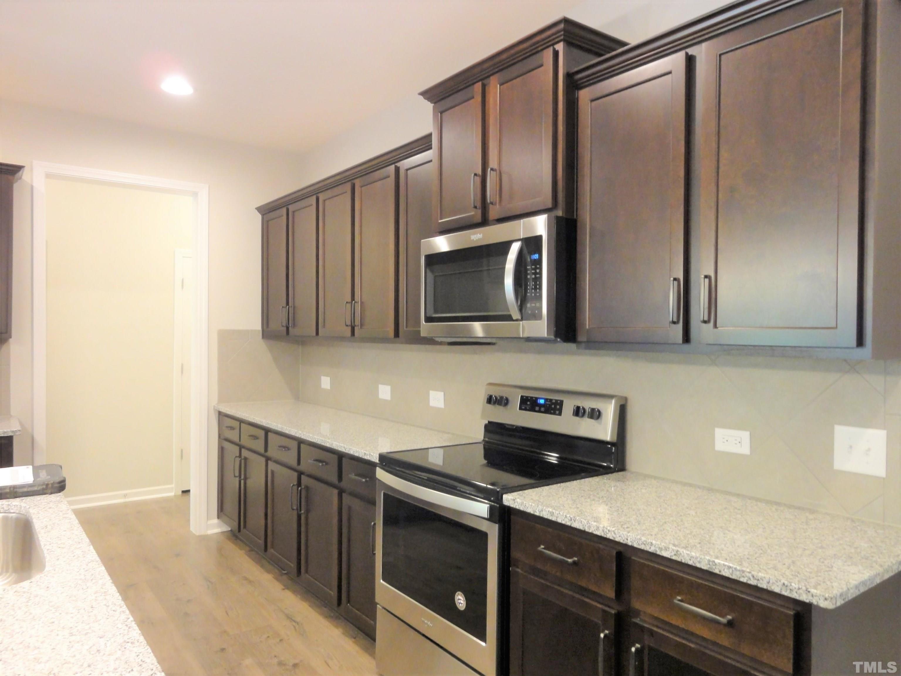 565 Metro Station Apex, NC 27502 - Photo 6 of 29 a kitchen with stainless steel appliances a sink a stove and a refrigerator with wooden floor