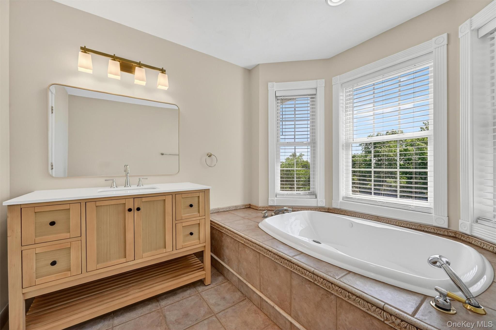 954 Ridgebury Road New Hampton, NY 10958 - Photo 25 of 45 This bathroom offers a relaxing retreat with a soaking tub, updated vanity, large mirror, and natural light from the surrounding windows. Located adjacent to the first-floor bedroom, this full bath creates a comfortable main-level ensuite option. Use it as your primary suite, or, if you prefer the second-floor primary, this space becomes a private and welcoming guest suite for family or visitors.