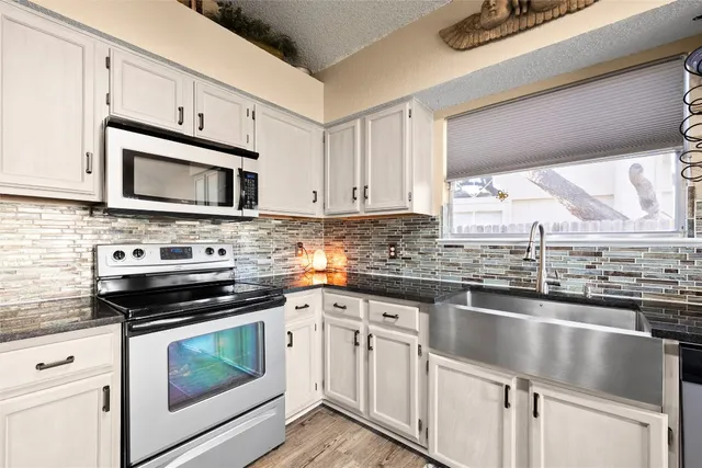 a kitchen with granite countertop a sink cabinets stainless steel appliances and a window