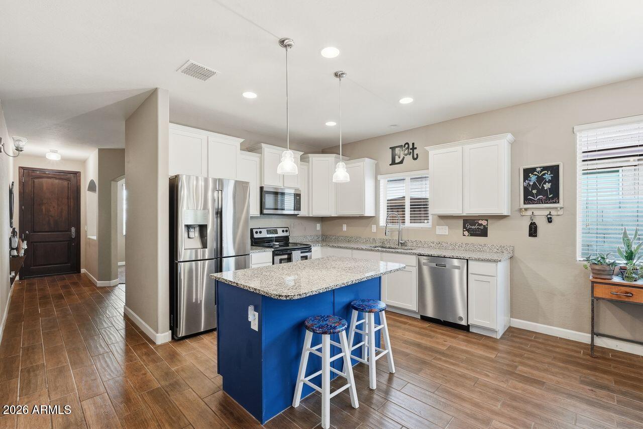 23602 West Ripple Road Buckeye, AZ 85326 - Photo 13 of 38 a kitchen with stainless steel appliances kitchen island granite countertop a refrigerator a sink dishwasher a stove and white cabinets with wooden floor