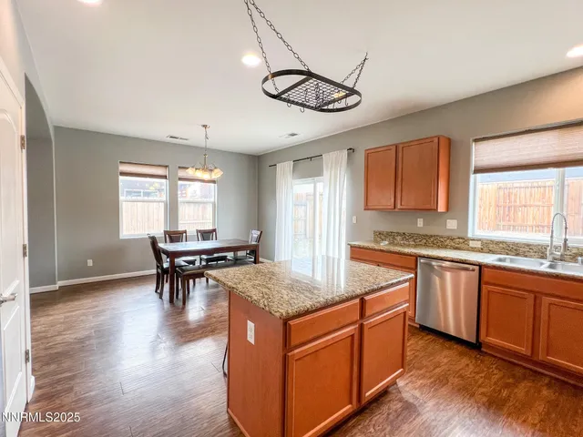 a open kitchen with stainless steel appliances granite countertop a stove top oven a sink dishwasher a dining table and chairs with wooden floor