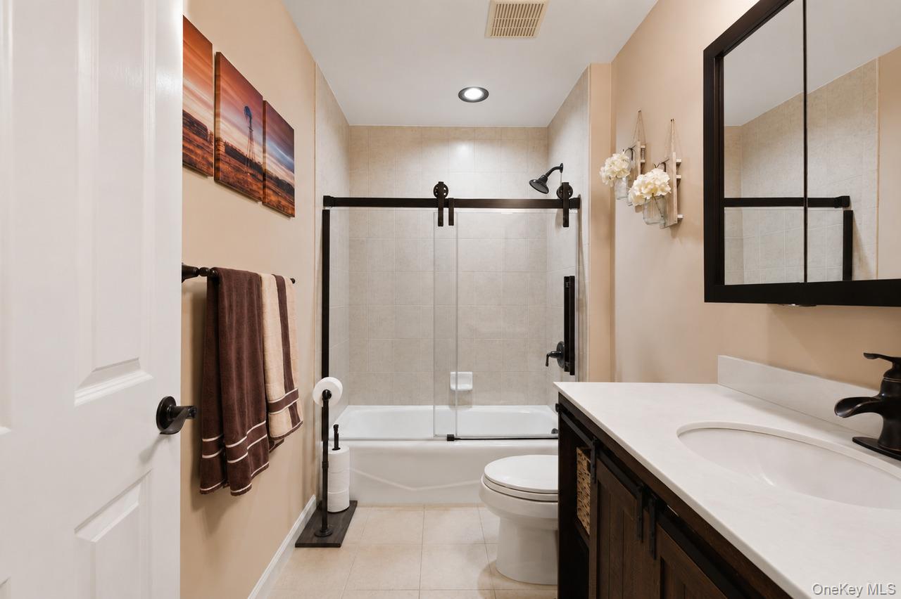 64 Roma Orchard Road Peekskill, NY 10566 - Photo 29 of 40 Bathroom featuring a white bathtub with a sliding glass door and dark bronze hardware, white vanity with an integrated sink and dark bronze faucet, dark wood-finish vanity cabinetry, and recessed lighting