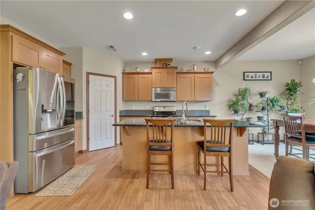 a kitchen with stainless steel appliances granite countertop a refrigerator a stove a sink a dining table and chairs with wooden floor