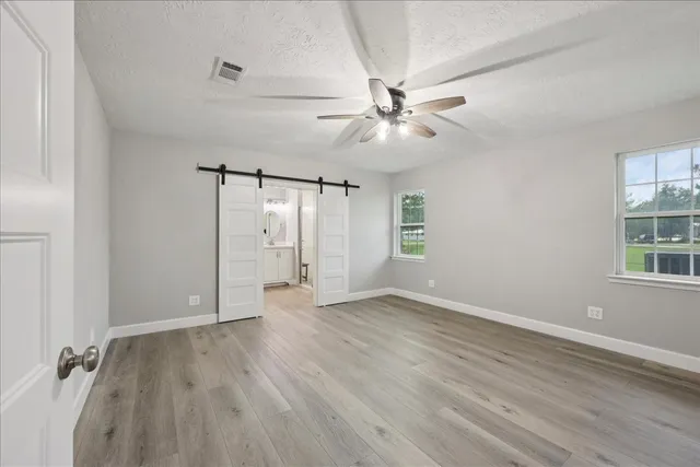 an empty room with wooden floor fan and windows