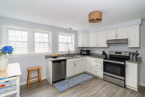 a kitchen with granite countertop a stove a sink dishwasher and white cabinets with wooden floor