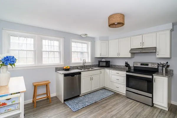 a kitchen with granite countertop a stove a sink dishwasher and white cabinets with wooden floor