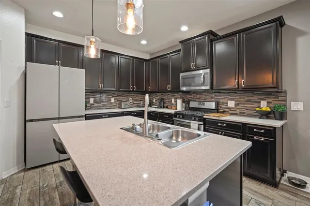 a kitchen with stainless steel appliances granite countertop a sink a stove a refrigerator and island with wooden floor