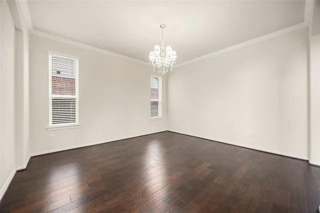 an empty room with wooden floor chandelier and windows