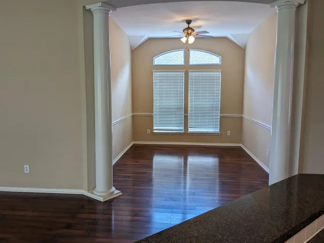 an empty room with wooden floor chandelier and windows