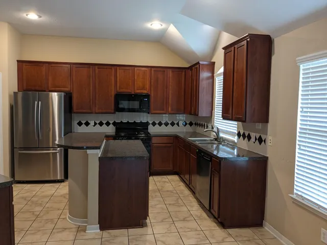 a kitchen with stainless steel appliances granite countertop wooden cabinets a stove a sink and a refrigerator