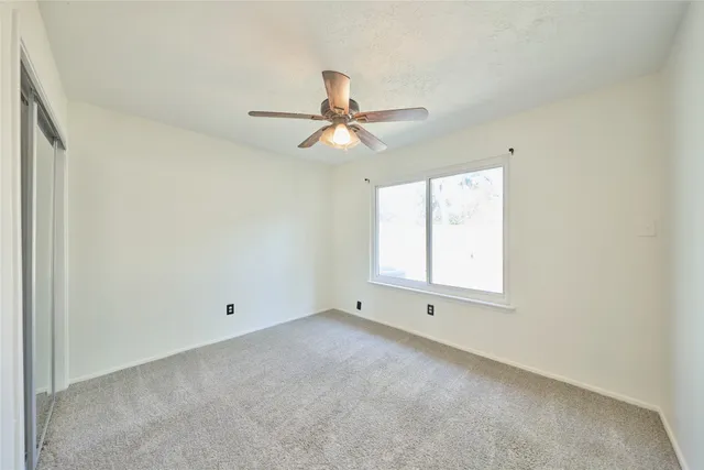 an empty room with chandelier fan and windows