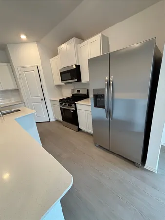 a kitchen with stainless steel appliances a refrigerator a stove a sink a microwave a refrigerator white cabinets and wooden floor