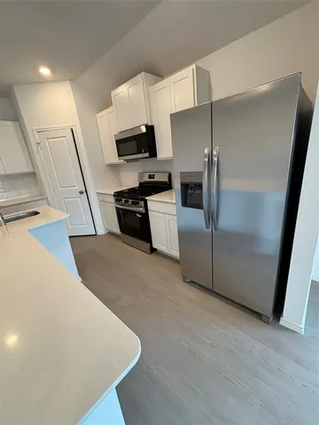 a kitchen with stainless steel appliances a refrigerator a stove a sink a microwave a refrigerator white cabinets and wooden floor