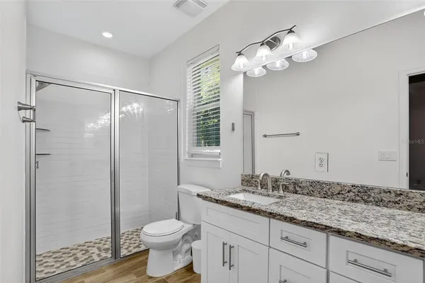 a bathroom with a granite countertop sink a toilet a mirror and shower