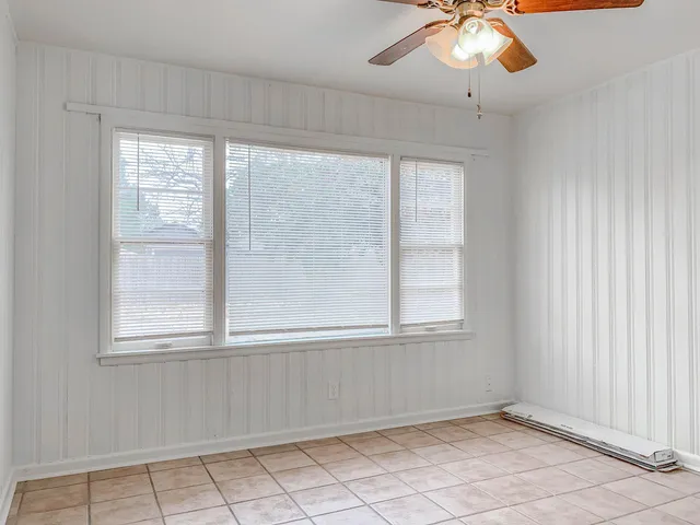 an empty room with chandelier fan and windows