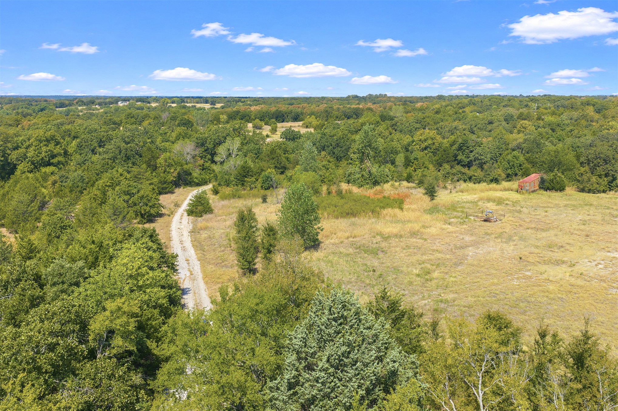 23922 Pickens Road Madill, OK 73446 - Photo 12 of 19 Rural landscape featuring a dirt road, mature trees, open fields, and a distant outbuilding