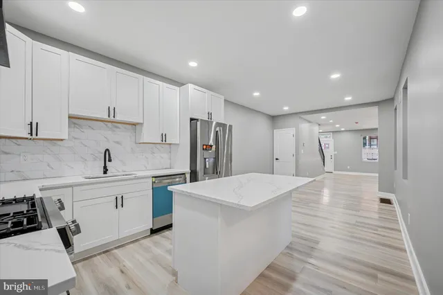 a large kitchen with stainless steel appliances kitchen island a sink dishwasher a refrigerator and white cabinets with wooden floor