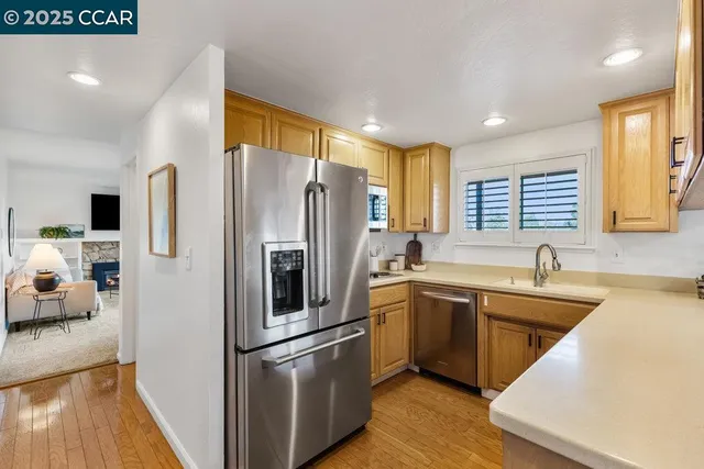 a kitchen with stainless steel appliances granite countertop a refrigerator a sink dishwasher a stove and white countertops with wooden floor