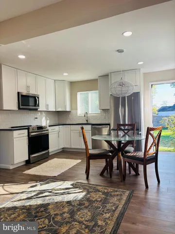 a kitchen with stainless steel appliances granite countertop a stove top oven a sink dishwasher a dining table and chairs with wooden floor