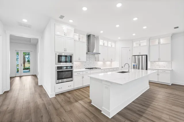 a large white kitchen with kitchen island a stove a sink dishwasher and white cabinets with wooden floor