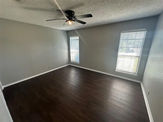 an empty room with wooden floor fan and windows
