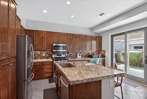 a kitchen with stainless steel appliances granite countertop a refrigerator a stove and a sink with wooden cabinets
