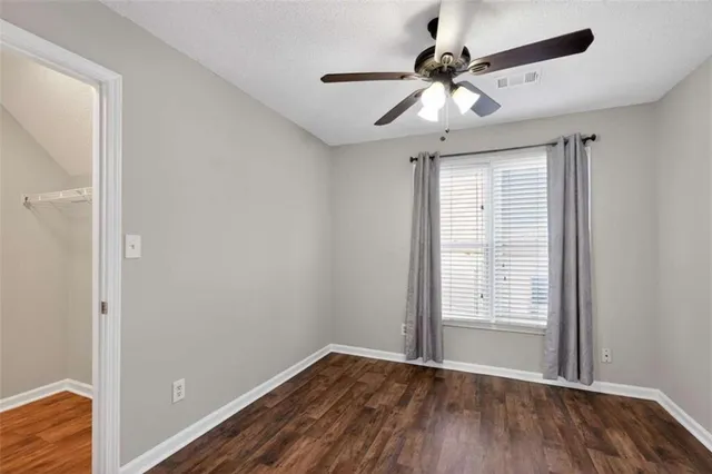an empty room with wooden floor chandelier fan and windows