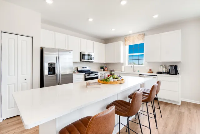 a kitchen with stainless steel appliances a dining table chairs refrigerator and microwave