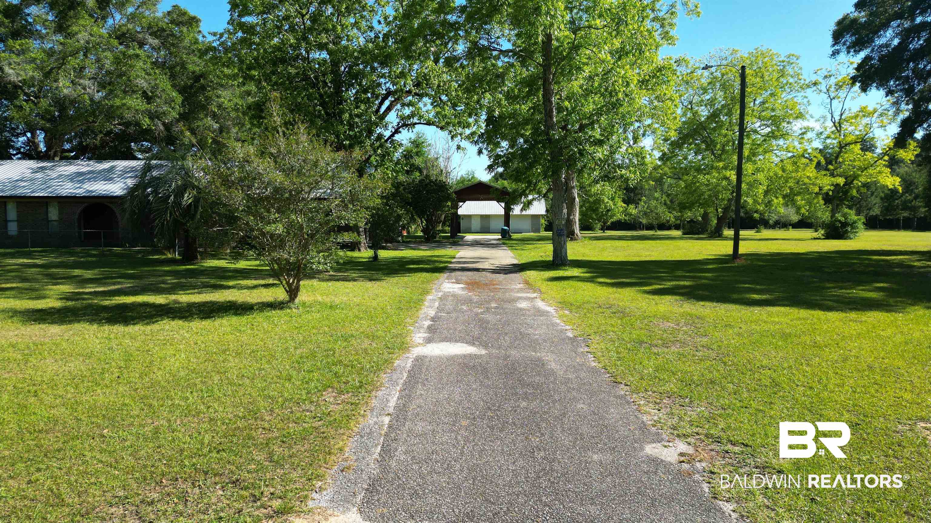 33370 Highway 98 Lillian, AL 36549 - Photo 6 of 58 Paved driveway leading to a residence with a metal roof, framed by mature trees and expansive lawn areas