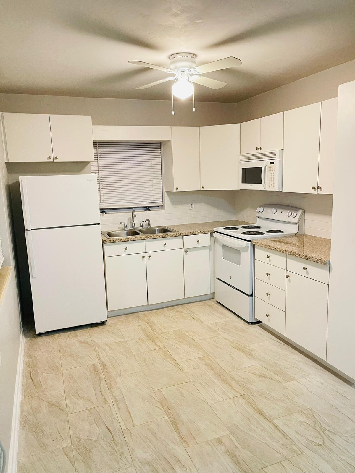 a kitchen with granite countertop a sink a stove a refrigerator and white cabinets