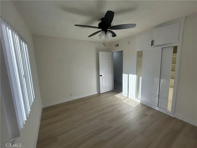 a view of an empty room with wooden floor and a ceiling fan