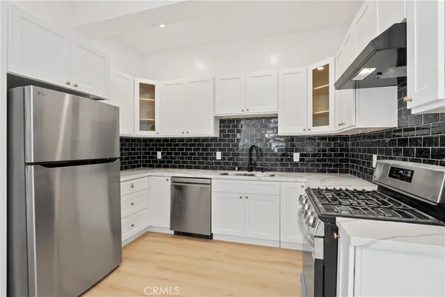 a kitchen with a refrigerator a stove a sink dishwasher and white cabinets with wooden floor