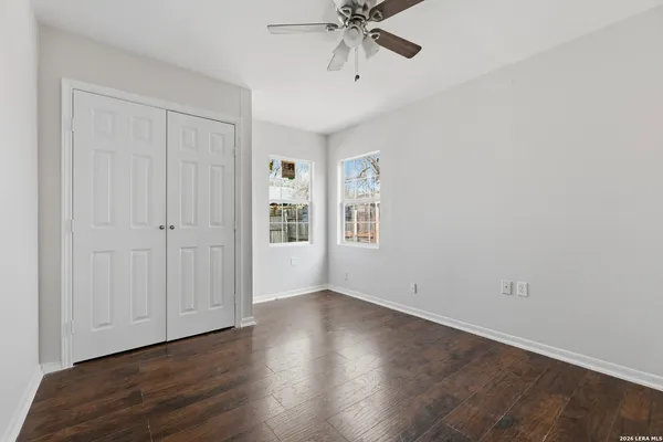 an empty room with wooden floor chandelier fan and windows