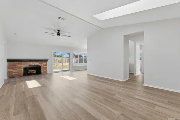 a view of an empty room with wooden floor fireplace and a window
